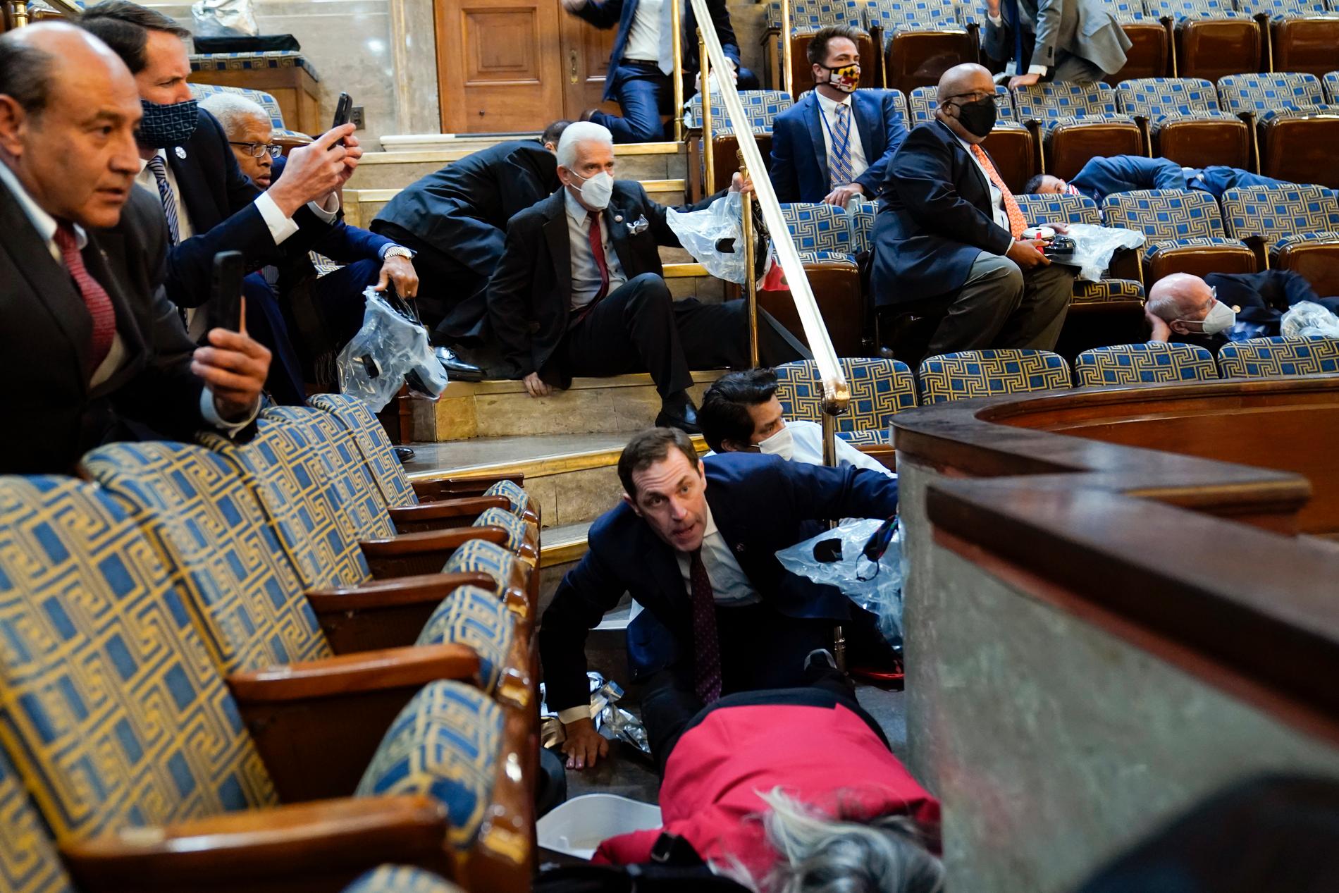 Personer hukar när stormare försöker ta sig in i representanthusets kammare. 