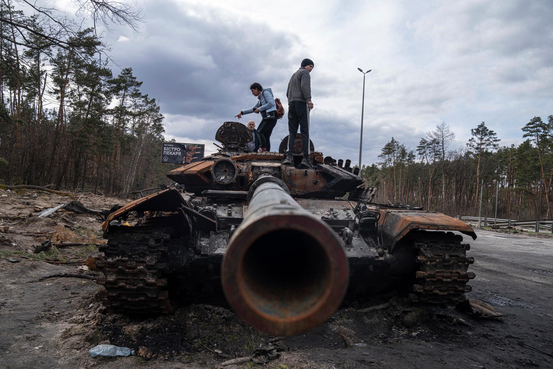 Lokalbor utanför Kiev står på en utslagen rysk stridsvagn.