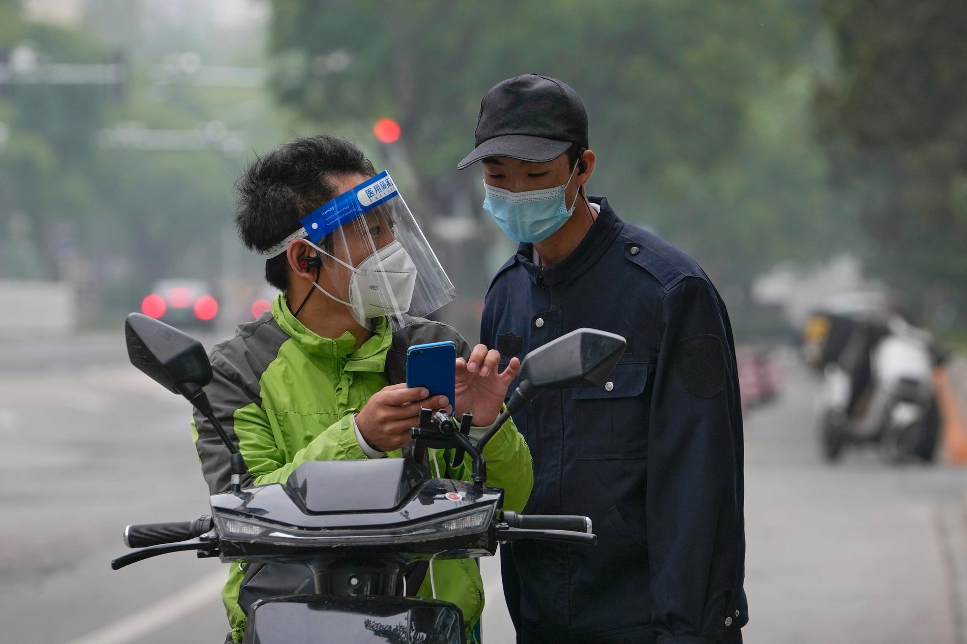 Ett varubud i Shanghai med andningsskydd och visir frågar en säkerhetsvakt om vägbeskrivning. Fotot är taget den 10 maj.