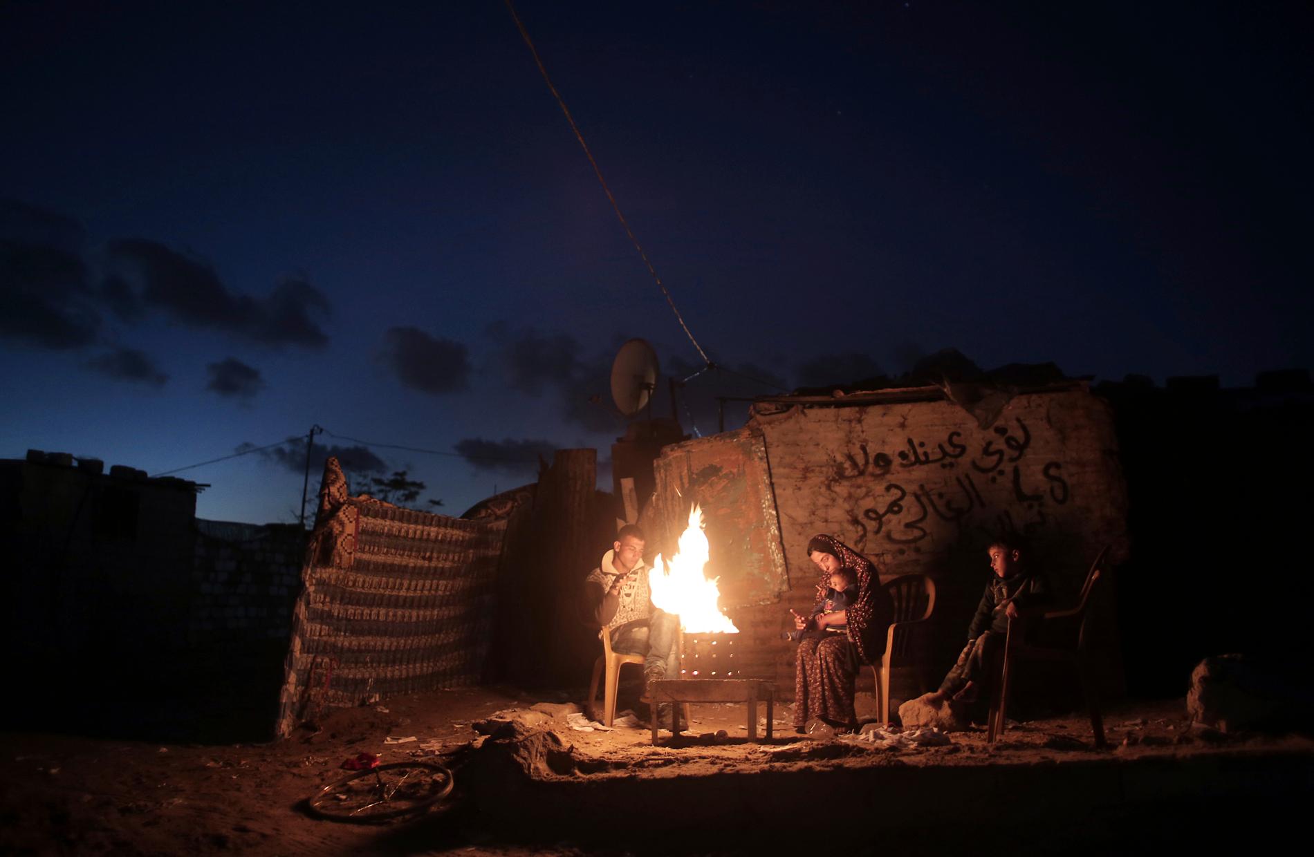 En familj värmer sig vid en öppen eld under ett strömavbrott i södra Gaza. Arkivbild.