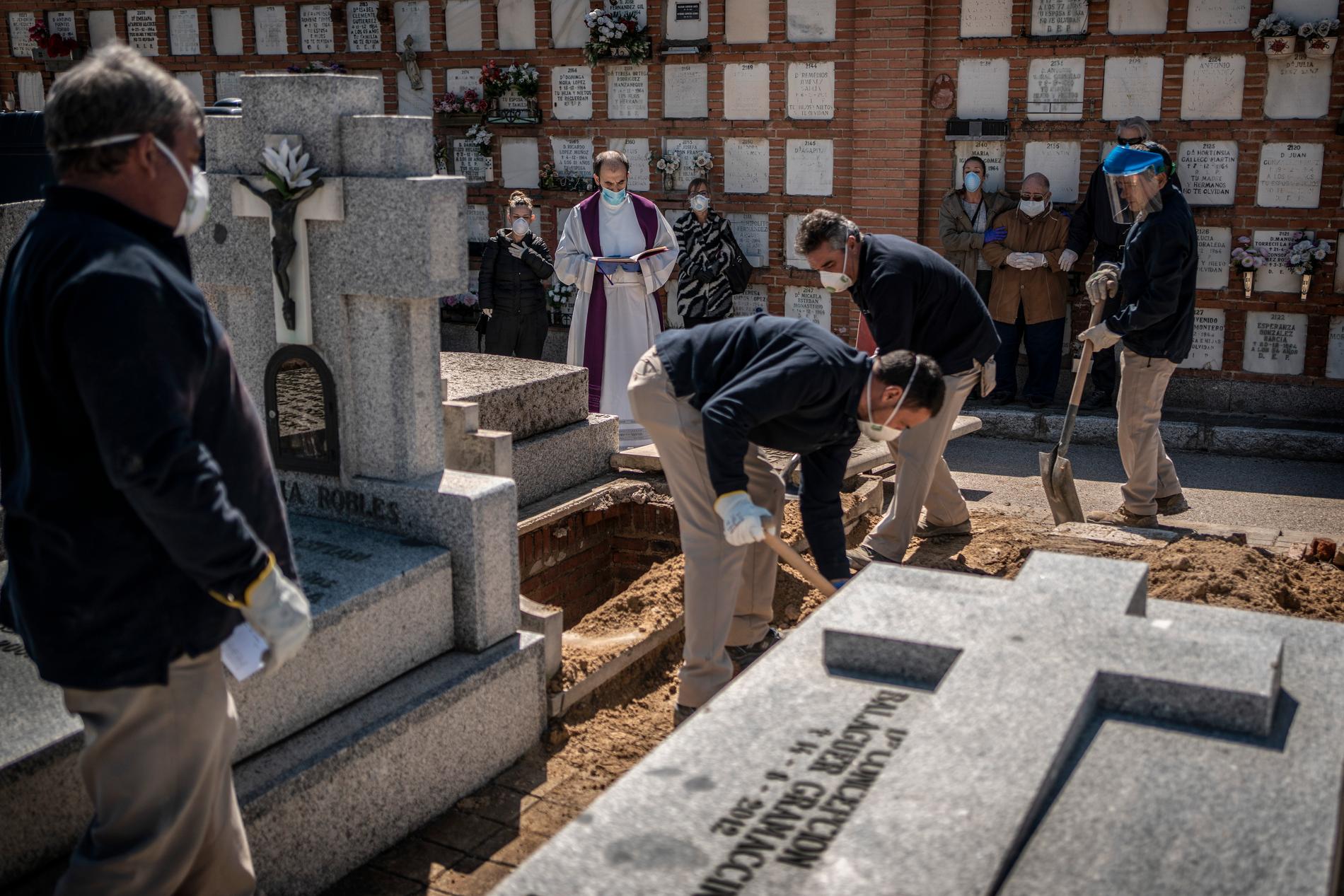 En präst och anhöriga ber en bön i samband med att en person som avlidit i covid-19 begravs på en kyrkogård i Madrid.