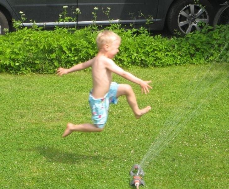 in underbart glada son Milton, 5 år, leker i vattenspridaren
