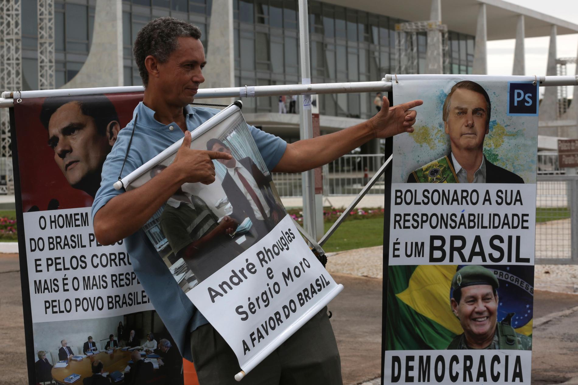 En anhängare av Jair Bolsonaro gör fingerpistoler framför affischer av honom, utanför presidentpalatset i Brasilia.
