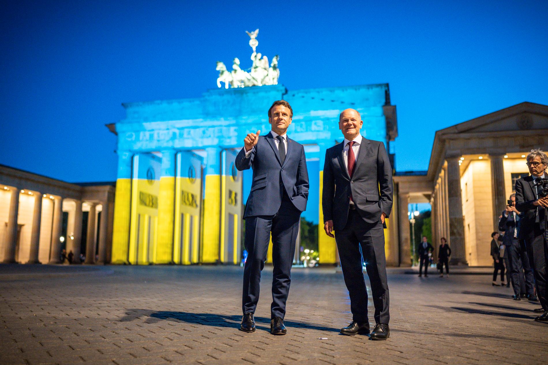 Emmanuel Macron och Olaf Scholz framför ett Brandenburger Tor i ukrainska färger. 