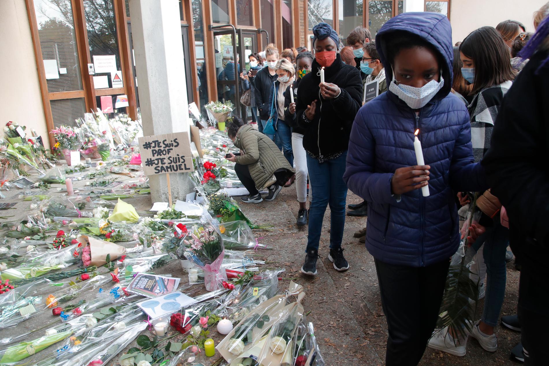 Blommor och tända ljus utanför skolan i Parisförorten Conflans-Sainte-Honorine, där en lärare mördades i fredags.