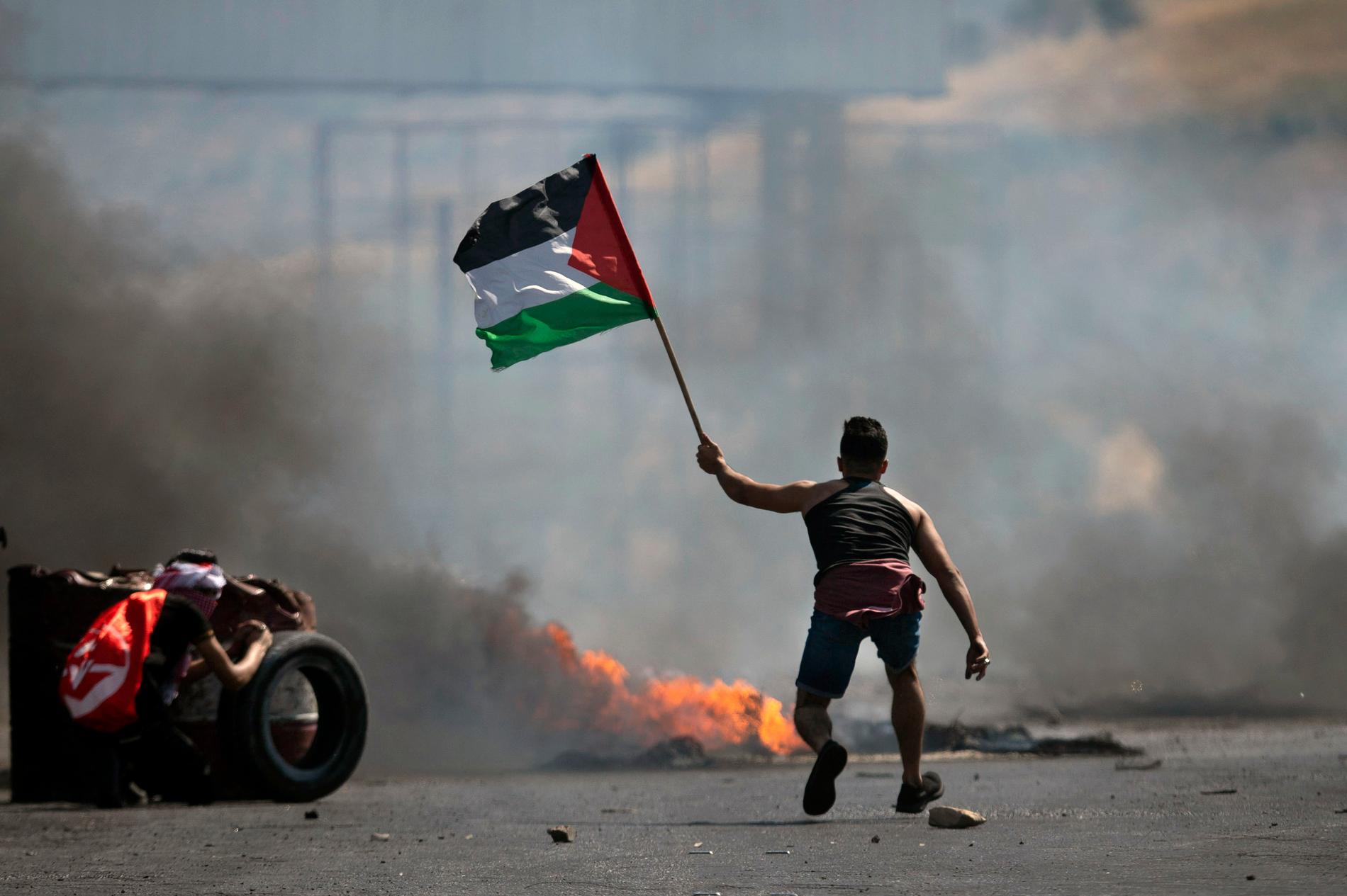 En demonstrant höjer en palestinsk flagga vid sammandrabbning med israeliska styrkor i närheten av Nablus, Västbanken 