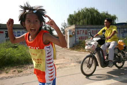 Rekordung löpare Zhang Huimin har sprungit 355 mil på två månader. I bakgrunden ses hennes pappa Zhang Jianmin – på moped.