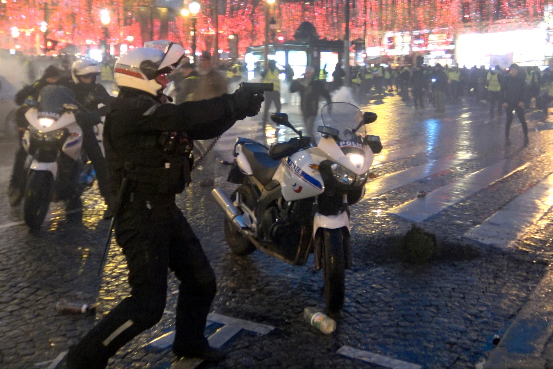 En polis riktade sitt vapen mot demonstranter vid Champs-Élysées i lördags.