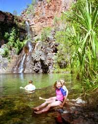 Rebecca Herbst tar ett dopp i lagunen vid Tjaynera falls. Två barn från södra Australien kopplar av nedanför de små pandanus-palmerna.