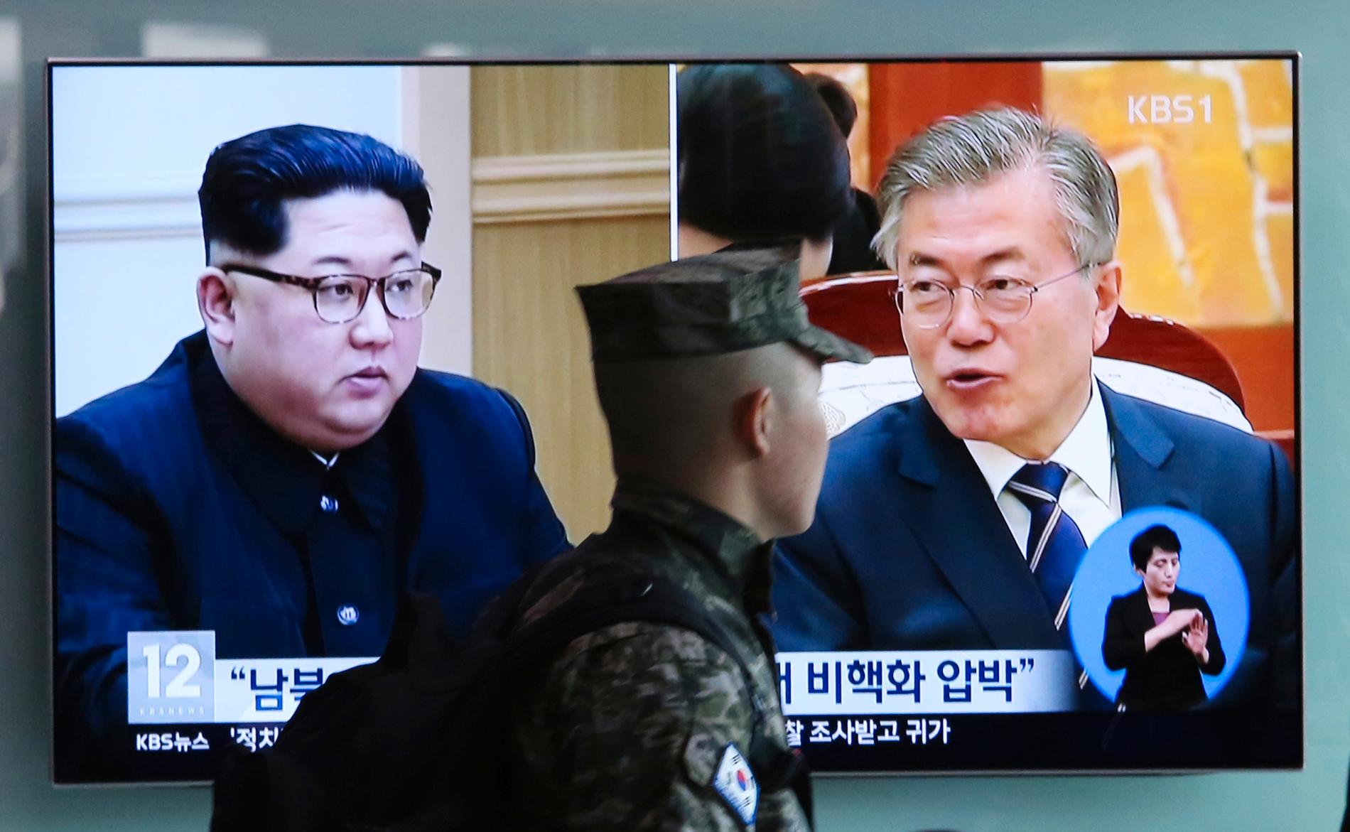 En sydkoreansk soldat passerar en tv-sändning som monterat ihop två bilder på Nordkoreas ledare Kim Jong-Un (till vänster) och Sydkoreas president Moon Jae-in. På fredag blir mötet mellan de båda ledarna verklighet.