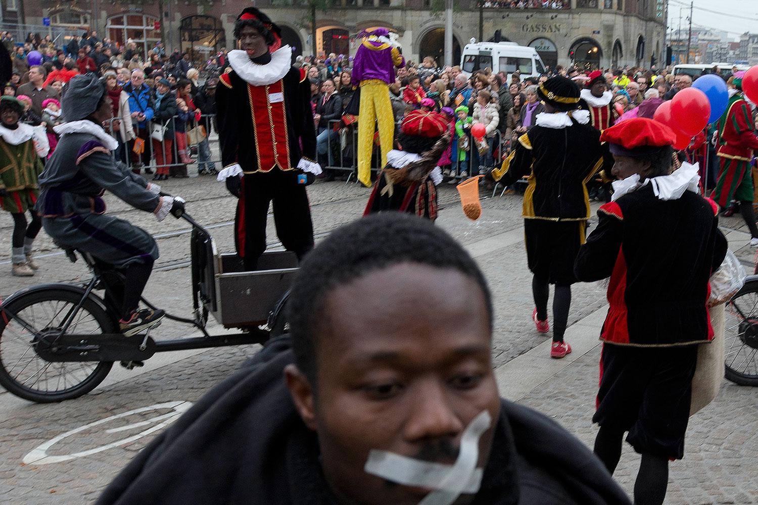 En julparad i Amsterdam med svartmålade ”Zwarte Piet”-figurer. I förgrunden en man som protesterar.