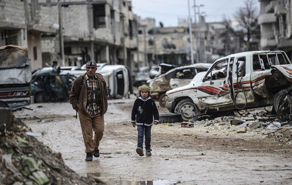 En kurdisk soldat och ett barn vandrar längs en av gatorna i den ödelagda staden.