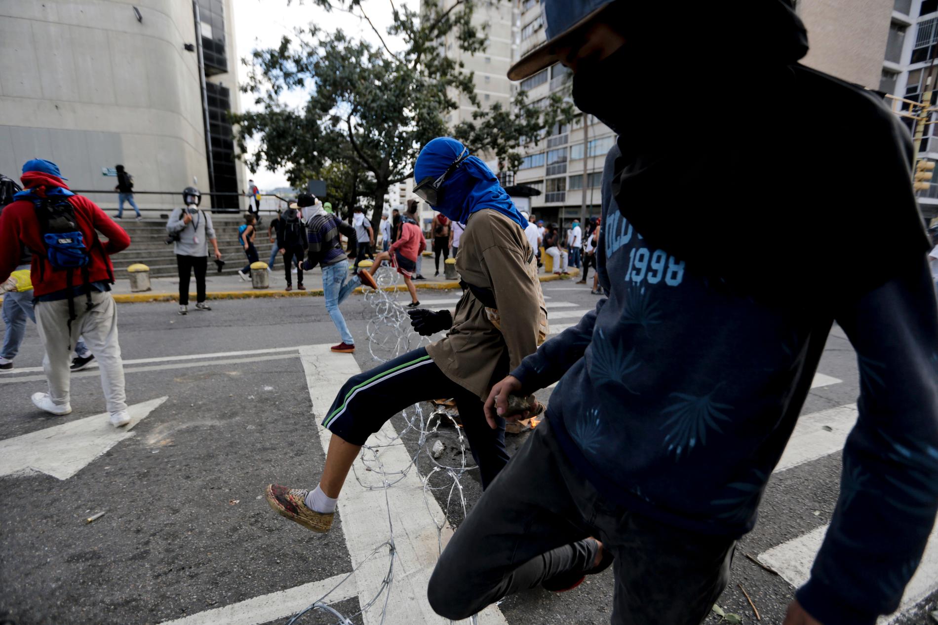 Demonstranter hoppar över en barriär av ståltråd i Caracas.