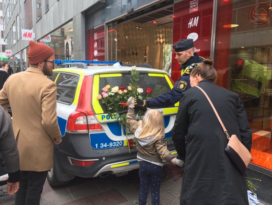 En flicka lägger blommor på en polisbil i Stockholm under lördagen.