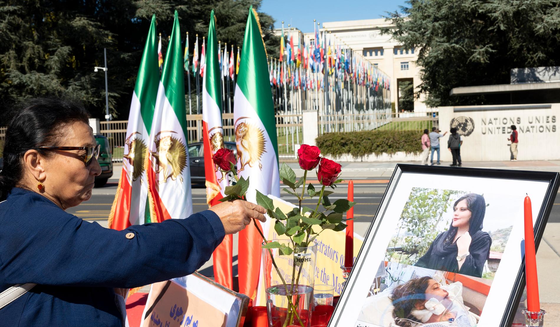 En person lägger blommor framför en bild på Mahsa Amini utanför FN-högkvarteret i Genève. 