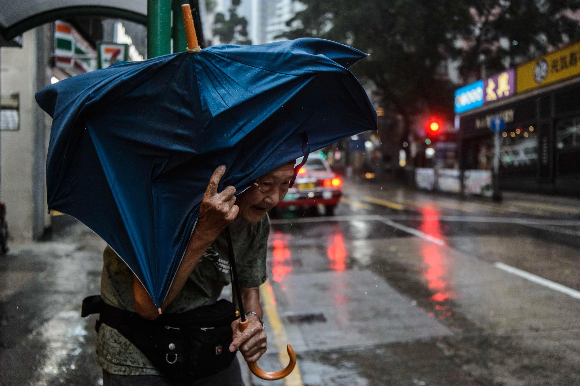 En äldre man söker skydd under ett paraply i väntan på en taxi i Hongkong samtidigt som tyfonen Mangkhut drar in. 