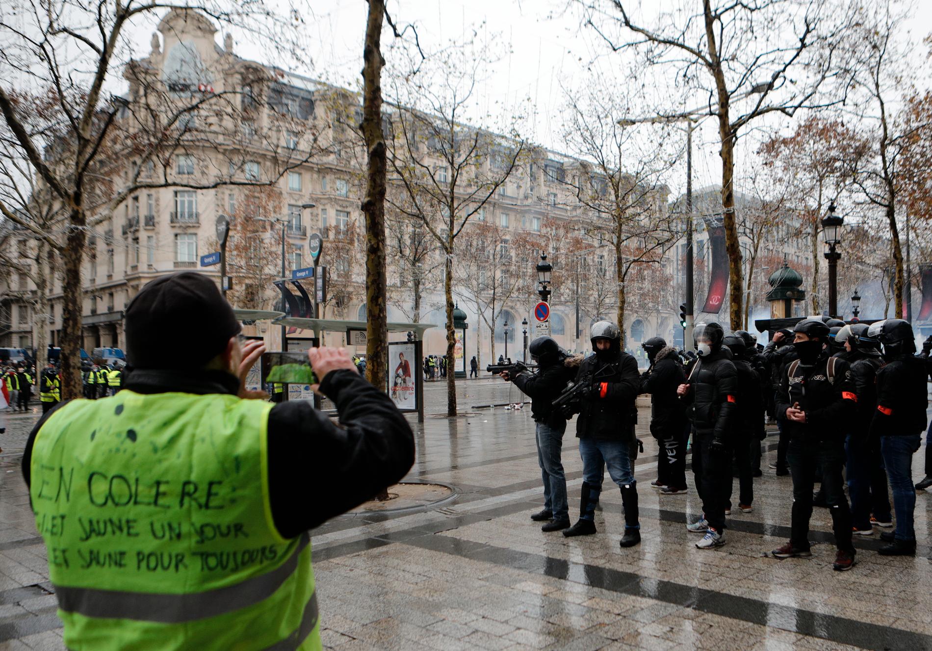 En demonstrant från proteströrelsen Gula västarna tar en bild av kravallpoliser på paradgatan Champs-Élysées i Paris på lördagen.