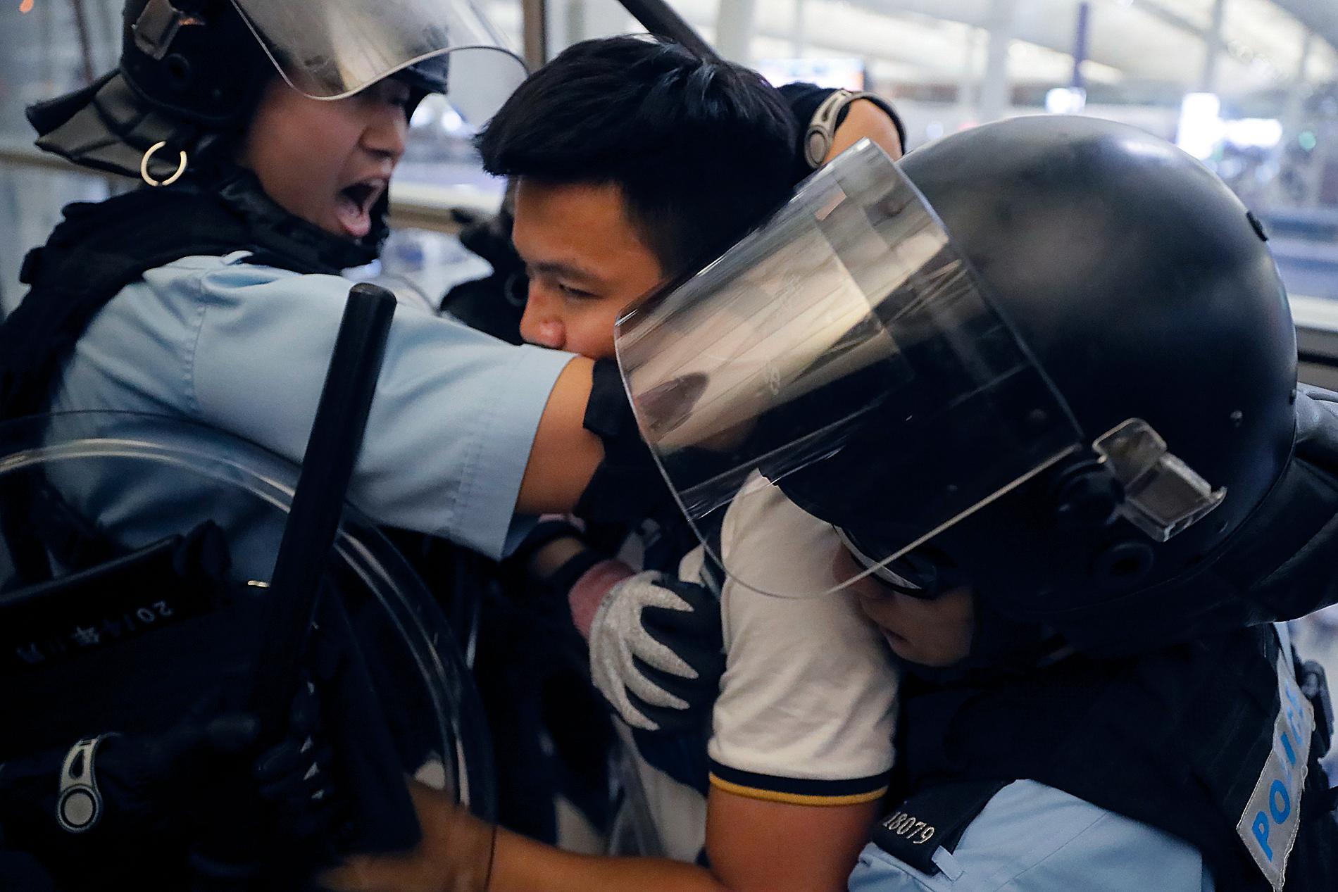 Poliser i kravallutrustning griper en demonstrant under tisdagens tumult på Hongkongs internationella flygplats.
