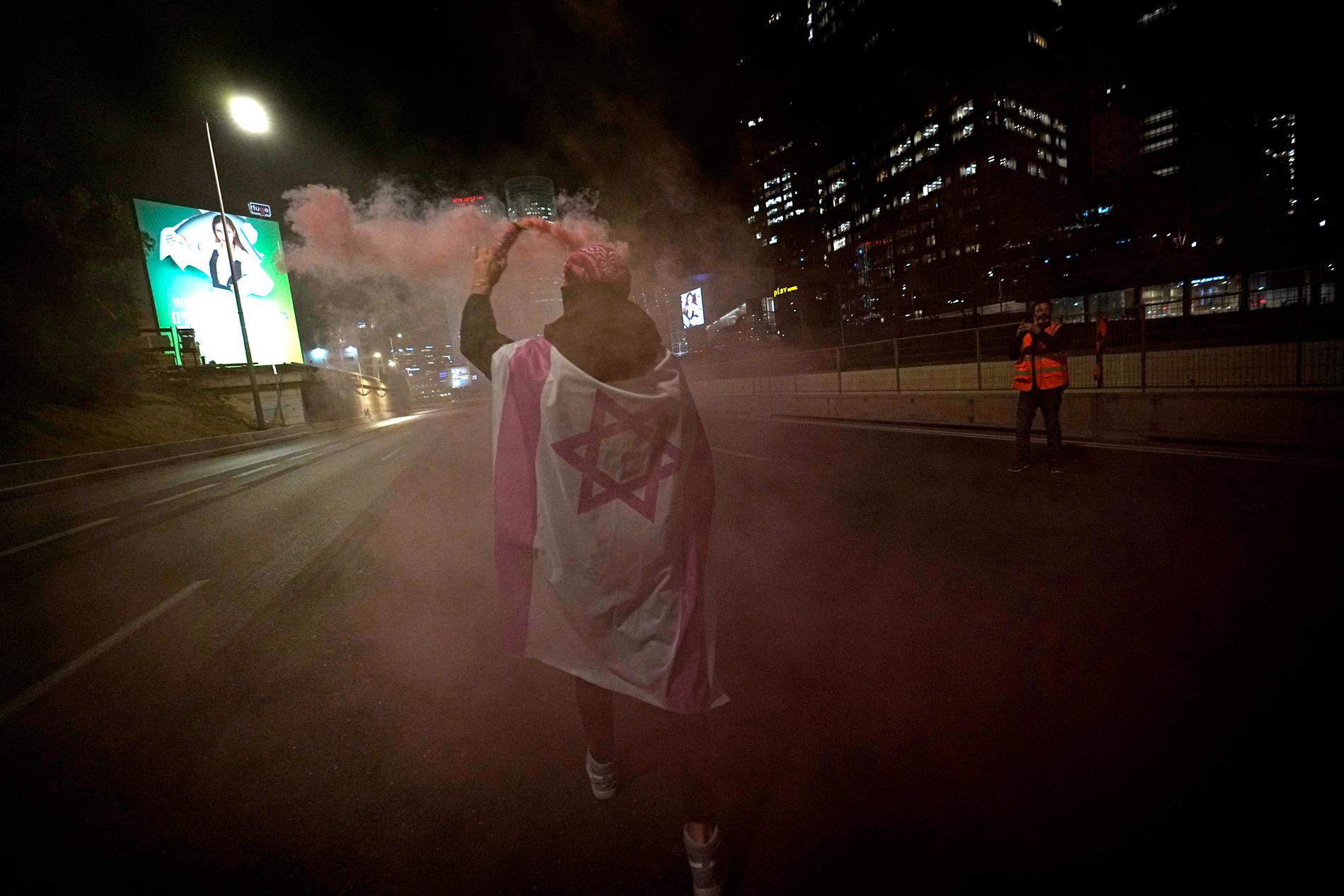 En israel bränner en rosa bloss när de blockerar en motorväg för att protestera mot planer från premiärminister Benjamin Netanyahus regering att se över rättssystemet,