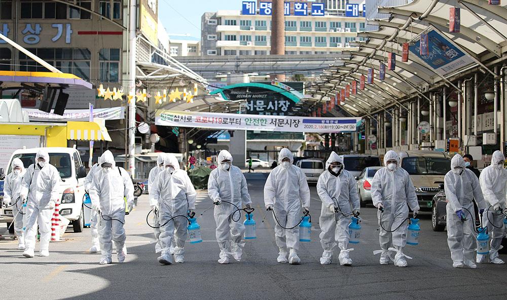 Arbetare i skyddskläder desinficerar ett marknadsområde i Sydkorea.