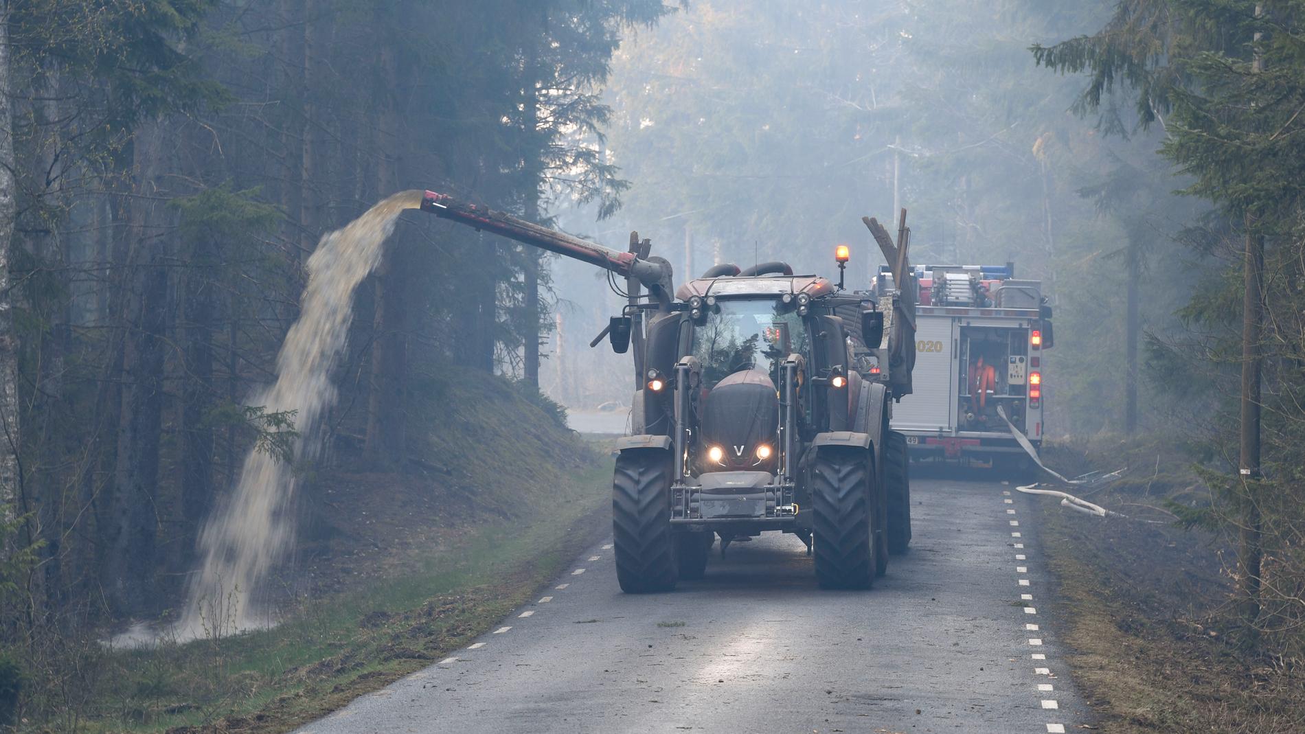 Hästveda tidigare i våras: Med hjälp av traktor och gödseltank vattenbegjuter en av traktens lantbrukare vägarna för att hindra skogsbrandens framfart. Arkivbild.